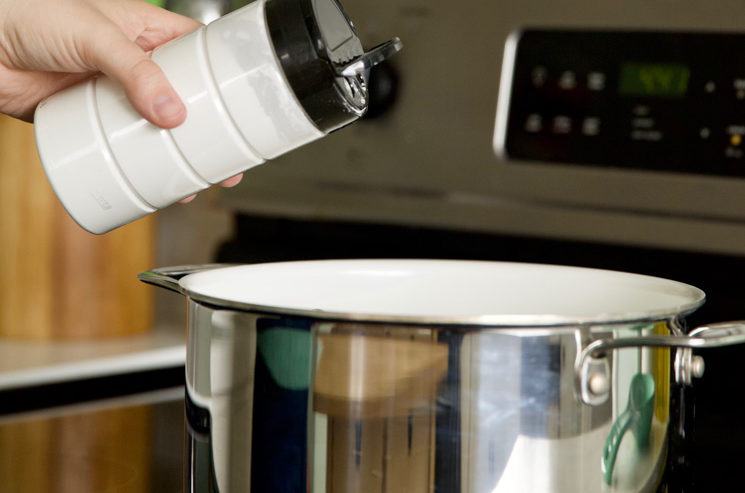 using a recycled parmesan cheese container to sprinkle cornstarch into a pot on a stove