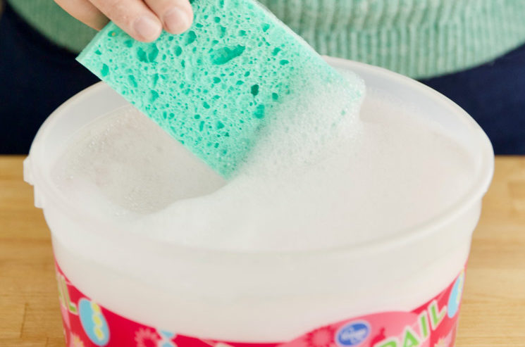 dipping a sponge into a recycled ice cream pail full of soapy water